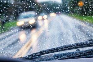 Driver POV (point of view) looking over the windshield wipers through the wet, blurry, partially opaque, partially transparent, spot speckled windshield of a car traveling on a rural highway during an autumn rain storm. Hazy, blurred headlights of approaching vehicle traffic are just blobs of light through the streaking and splattered raindrop water. Canon 5D Mark III.