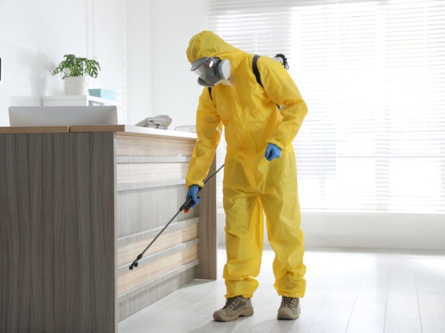 pest controller in protective suit sanitizing office.