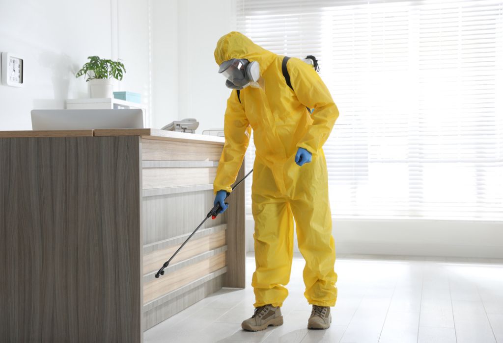 pest controller in protective suit sanitizing office.