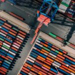 A panoramic view of Spare Parts in Barcelona bustling maritime scene, featuring ships docked at the port against a backdrop of vibrant city architecture and a clear blue sky.