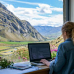 Digital nomad working on a laptop in a remote location with Canada's stunning landscapes, showcasing the lifestyle enabled by the Canada Digital Nomad Visa.